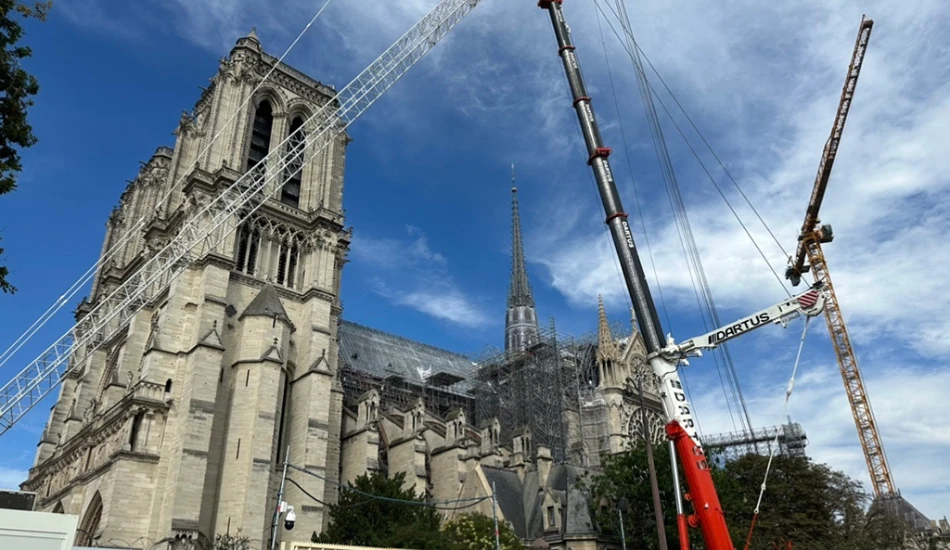 Restoration work is in progress at Notre Dame Cathedral, with cranes against a blue sky.
